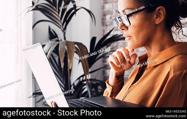 Side view of female people reading and using laptop computer concentrated. Smart working at home. Adult woman with eyewear working online