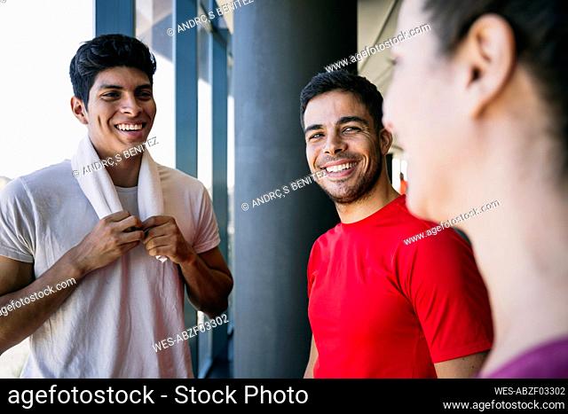 Smiling male athletes talking with woman while standing in gym during break