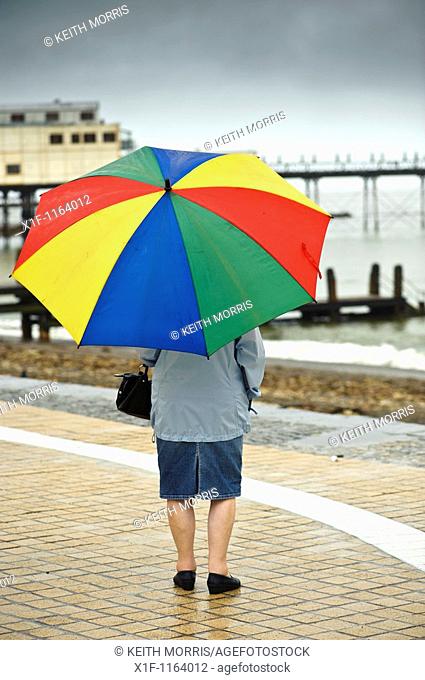 Rear view of a woman sheltering under an umbrella on Aberystwyth promenade in the rain july wet summer afternoon, Wales UK