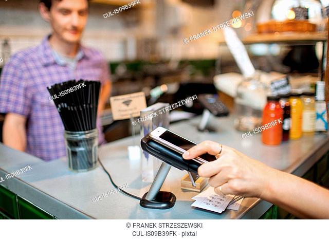 Cropped shot of female customer using smartphone contactless payment in cafe