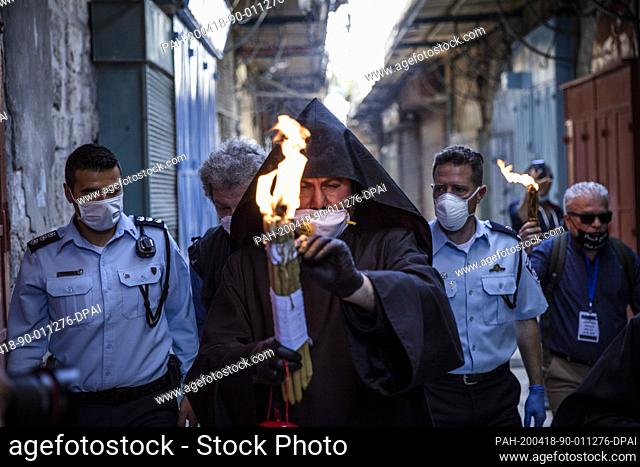 dpatop - 18 April 2020, Israel, Jerusalem: An Armenian priest holds a lit torch taken from the flame that supposedly appears miraculously in the Church of the...