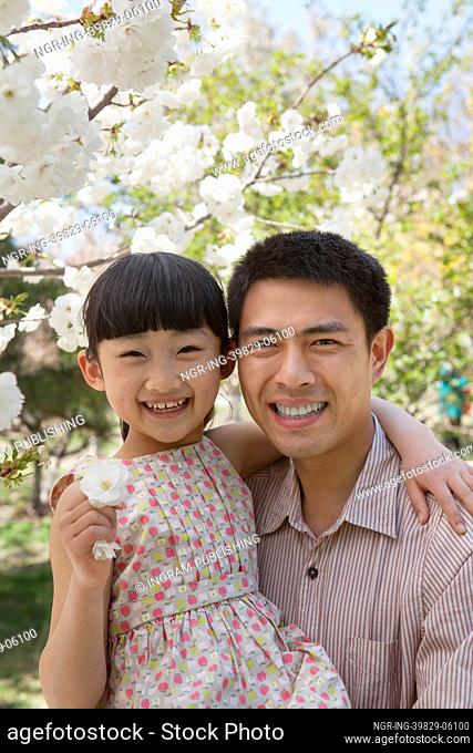 Smiling father and daughter enjoying the cherry blossoms on the tree in the park in springtime, portrait