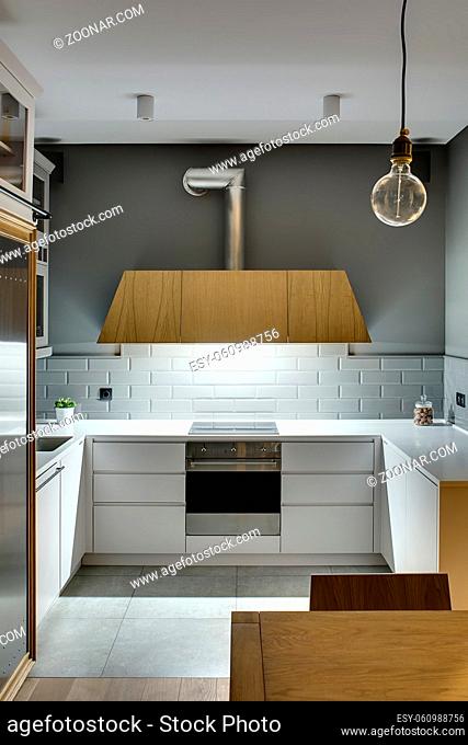 Design kitchen in a modern style with gray walls and white lockers and shelves. There is a glowing wooden kitchen hood, stove, oven, sink, fridge