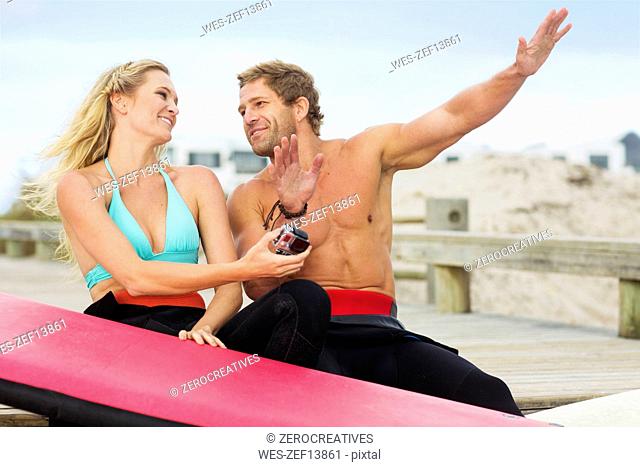 Happy couple with surfboard talking on the beach