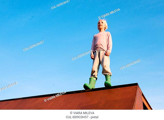 Boy standing on top of skateboard ramp against blue sky, low angle view