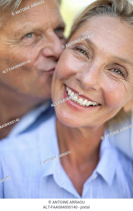 Mature woman smiling as man kisses her cheek, portrait