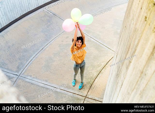 Woman with arms raised holding balloons standing on footpath
