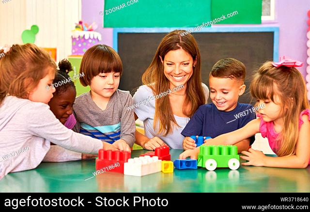 Kinder und Erzieherin in der Kindertagesstätte oder Vorschule spielen mit Bausteinen am Tisch