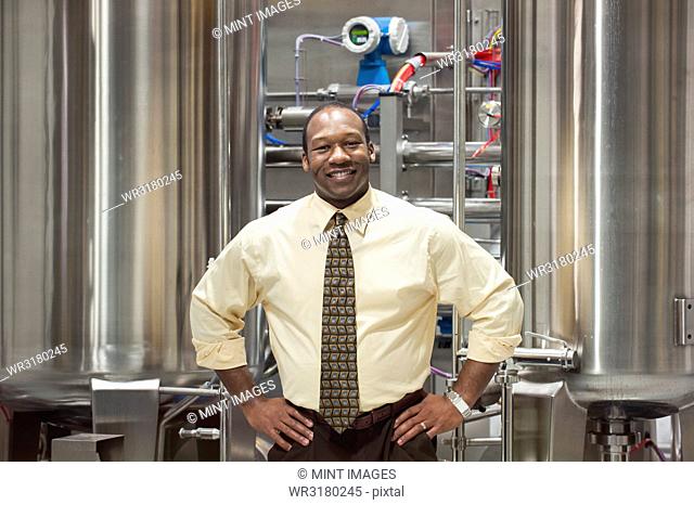 African American male management person in a shirt and tie standing in front of processing tanks in a bottling plant