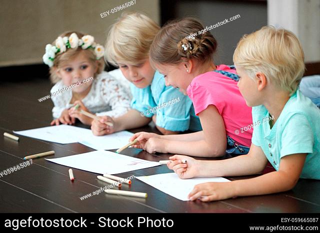 Cute little children friends drawing with pencils at home laying on floor