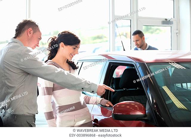 Car dealer pointing the interior of a car with a woman in a car shop