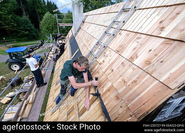 27 July 2023, Saxony, Seiffen: Remi Crouzet (front) from France restores the shingle roof of the rafters' dwelling in the Seiffen Open-Air Museum together with...