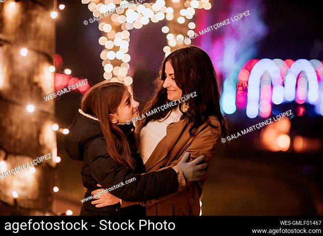 Smiling woman embracing daughter by illuminated lights