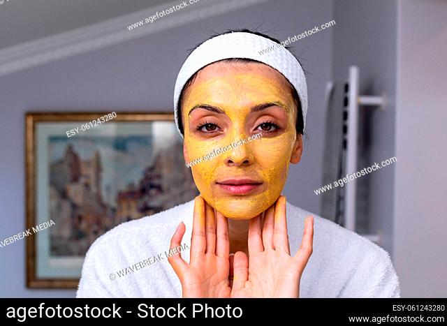 Portrait of caucasian young woman applying facial mask in bathroom at home