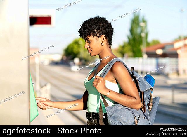 Young woman carrying backpack while using ticket machine
