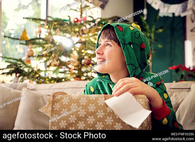 Smiling boy looking away while holding gift box during Christmas at home