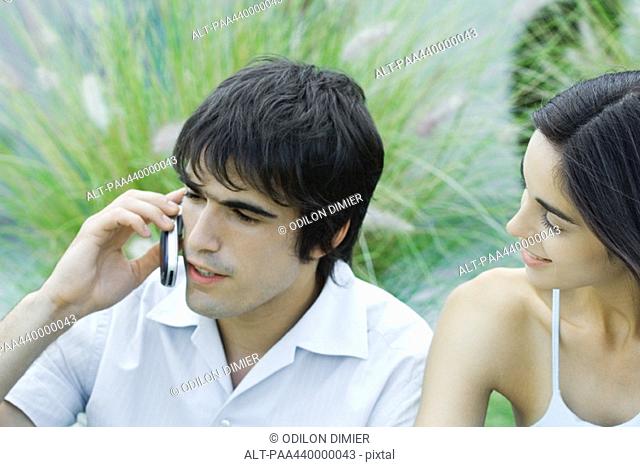 Young man using cell phone while girlfriend waits