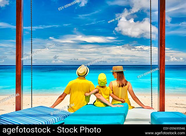 Family on beautiful Petite Anse beach, young couple in yellow with three year old toddler boy. Summer vacation at Seychelles, Mahe