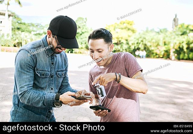 Two happy friends looking at a cell phone in the street, Two smiling friends looking at media on the cell phone in the street