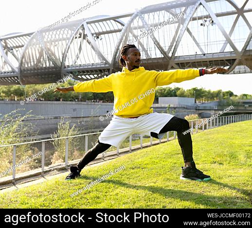 Male athlete practicing warrior pose while exercising against walkway