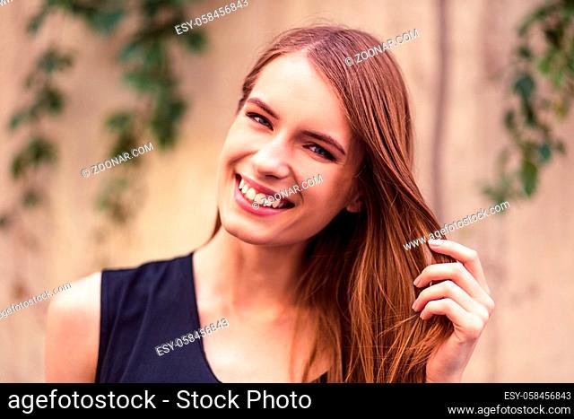 Smiling attractive girl touching hair. Young woman with open smile, white teeth and clean skin smiling for camera. Toned image