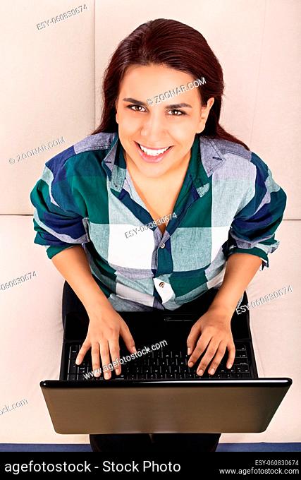 Home office concept. Internet communication concept. Beautiful happy and smiling young woman sitting on a sofa, working on computer at home