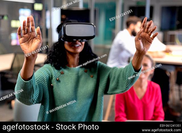 Smiling young african american businesswoman wearing virtual reality simulator gesturing in office
