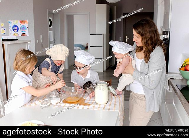 Mother carrying boy with children preparing dough in kitchen