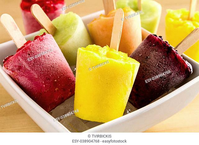 Close up of assorted flavors of homemade fresh pureed frozen fruit popsicles in white bowl with ice