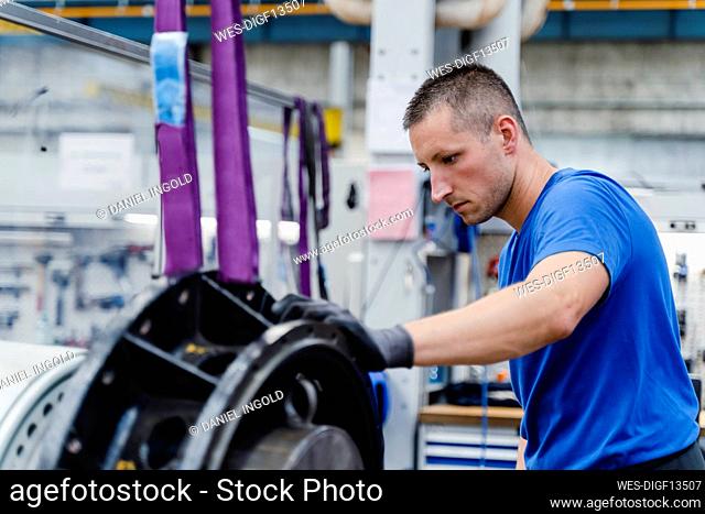 Male manual worker concentrating while doing quality check of machinery at illuminated factory