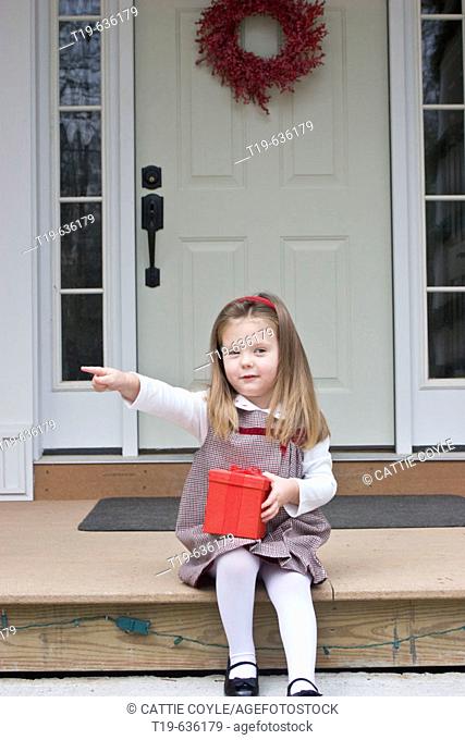 Three year old girl sitting on the porch of her family's house in Woodstock, CT, holding a Christmas present. USA