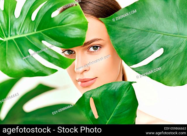 Close up portrait of young beautiful woman with perfect smooth skin in tropical leaves. Natural cosmetics, skincare, spa concept