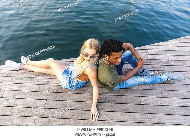 Multicultural young couple relaxing back to back on jetty