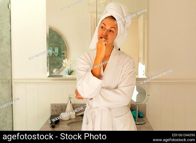 Happy caucasian woman wearing robe, brushing teeth in bathroom
