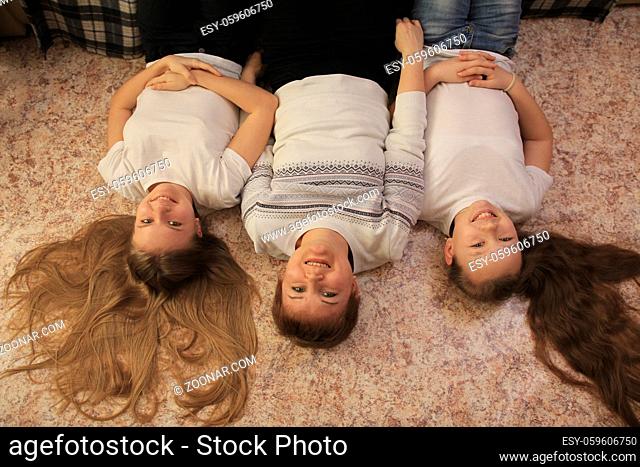 Portrait of young mom and her two teen daughters lying on the floor at home, concept of family relations