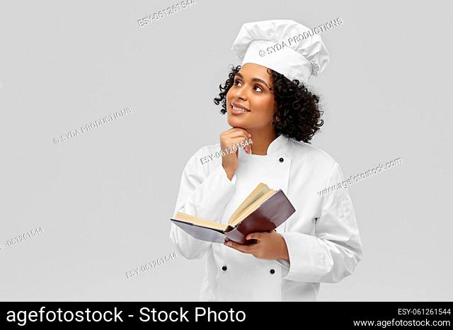 happy female chef in white toque reading cook book