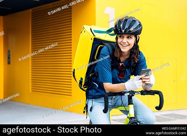 Happy delivery person wearing cycling helmet sitting on bicycle