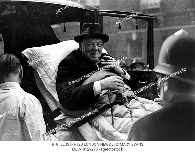 Winston Churchill (1874-1965), English politician, having a cheeky puff on his cigar whilst being stretchered from his London flat to a West End nursing home...