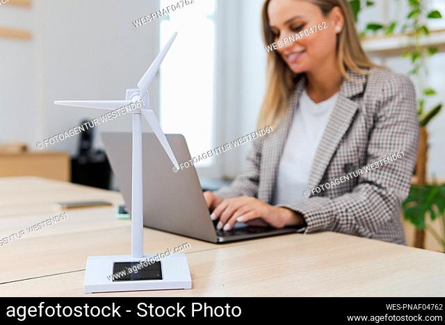 Young businesswoman using laptop and digital tablet at desk with wind turbine model in foreground