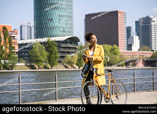 Thoughtful businesswoman with bicycle walking by River Main on sunny day