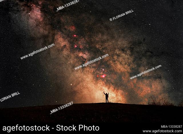 Silhouette of a person with his hands raised in front of the galactic center of Michstrasse