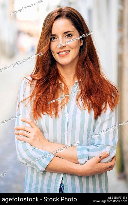 Smiling redhead woman with arms crossed standing outdoors