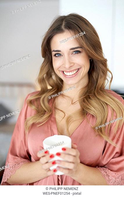 Portrait of smiling young woman in dressing gown holding cup of coffee