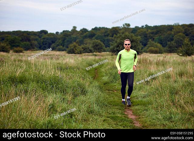 Fit muscular man jogging on a rural trail through grassland wearing sportswear and sunglasses in an active lifestyle concept