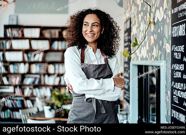 Young entrepreneur wearing apron looking away while standing at cafe