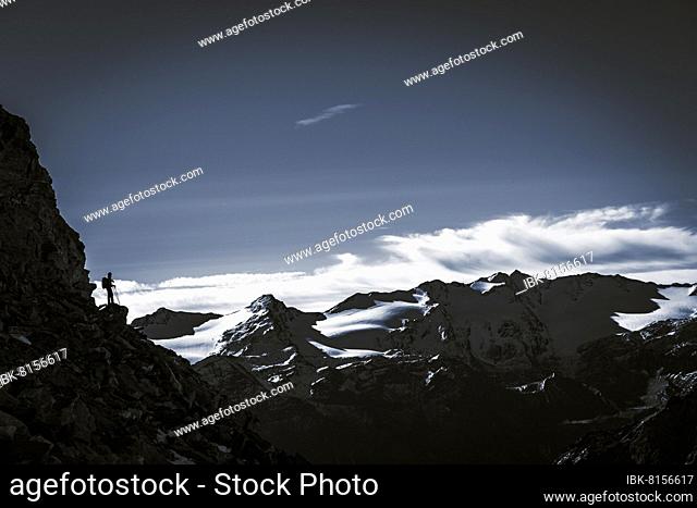 Climber on rocky outcrop with South Tyrolean mountains at blue hour, Martell Valley, Naturno, South Tyrol, Italy, Europe
