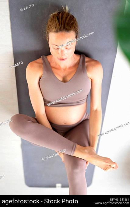 Young beautiful pregnant woman training pilates at home in her living room. Healthy lifestyle and active pregnancy and motherhood concept