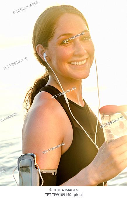 Smiling woman wearing headphones holding water bottle