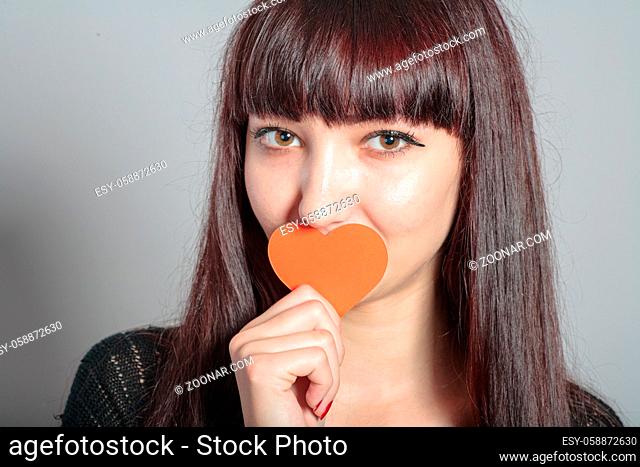 Woman is holding paper heart in front of her mouth, head and shoulders shot