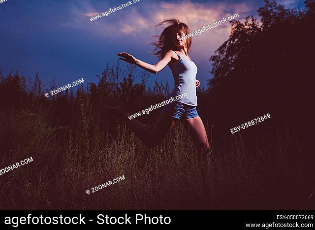 Joyful girl is running away in the tall grass. Copyspace is on the sky